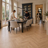 Natura Visgraat Warm Oak Klik PVC – sfeerbeeld: eetkamer met lange zwarte tafel en servieskast, gezin dekt de tafel