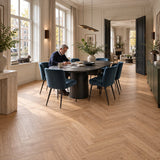 Natura Visgraat Warm Oak Klik PVC – sfeerbeeld: lichte eetkamer aan de gracht, man schrijft aan ovale tafel